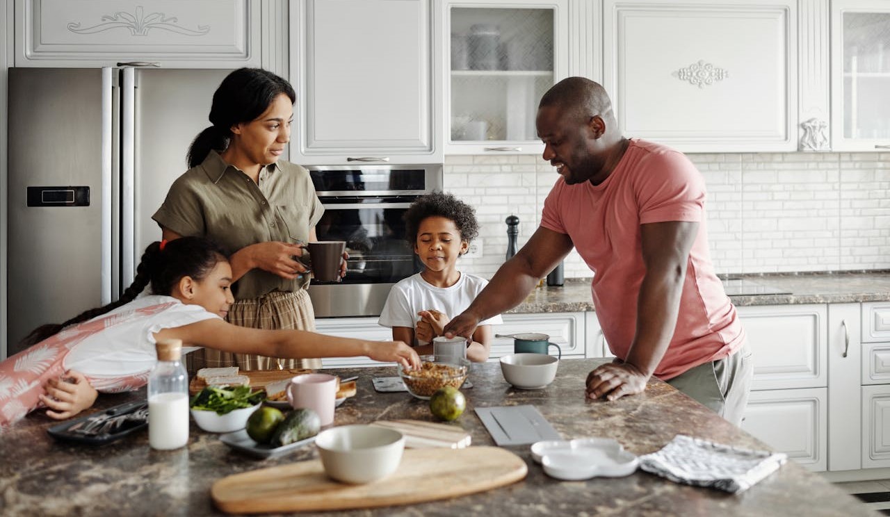 Family with two small children looking happy gathered around kitchen island enjoying coffee and snacks.